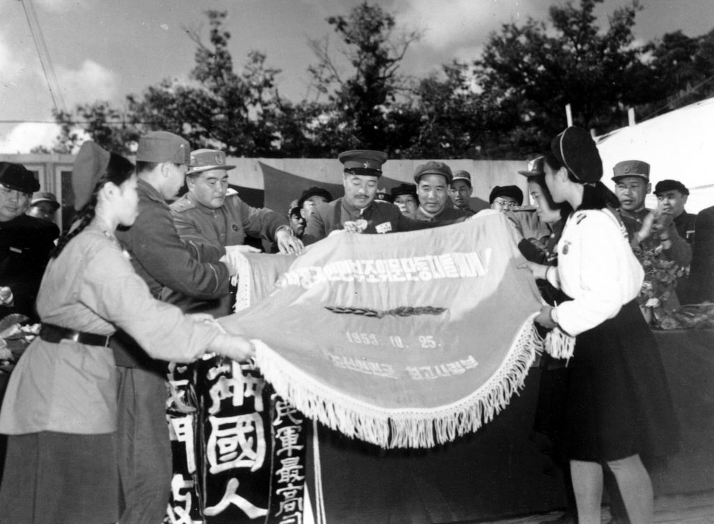 1953年10月，中国人民志愿军参谋长李达（左五）陪同中国人民第三届赴朝慰问团总团长贺龙（左四）与朝鲜人民军最高司令部互赠锦旗。